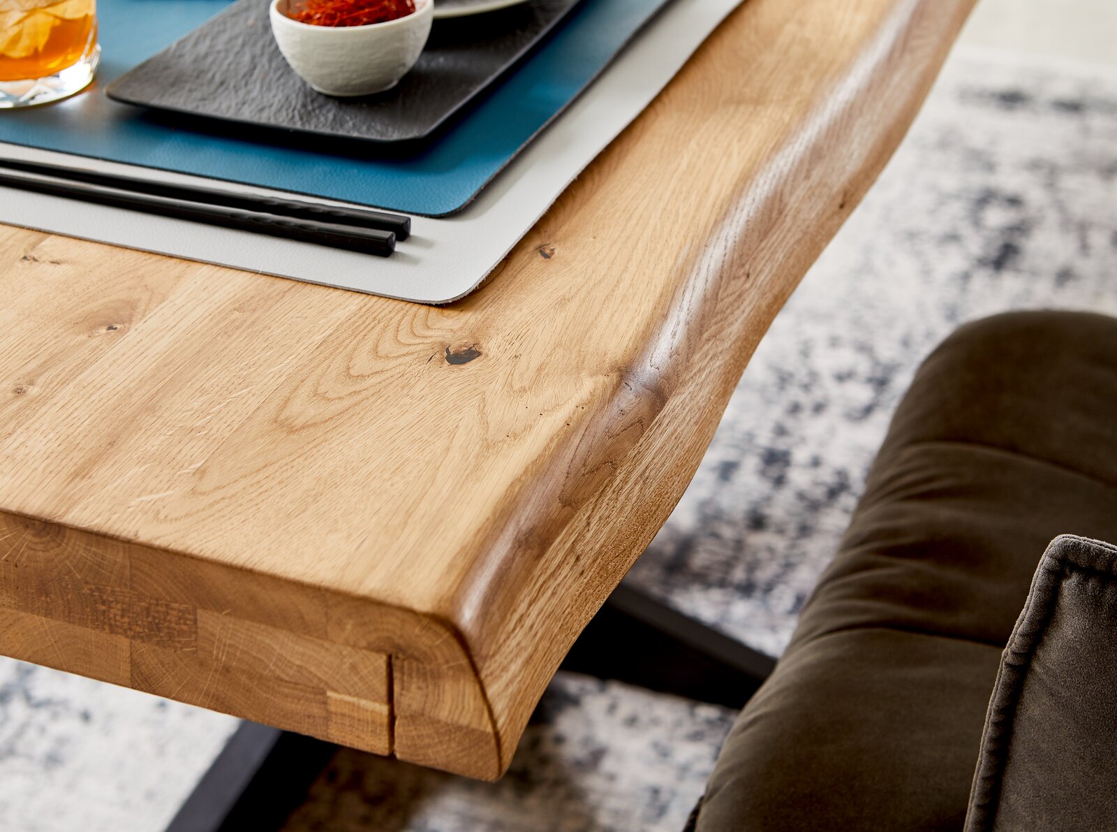 Nahaufnahme eines Esstisches aus Holz mit natürlicher Kante, darauf Tischsets und Geschirr, seitliche Perspektive.