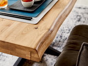 Nahaufnahme eines Esstisches aus Holz mit natürlicher Kante, darauf Tischsets und Geschirr, seitliche Perspektive.