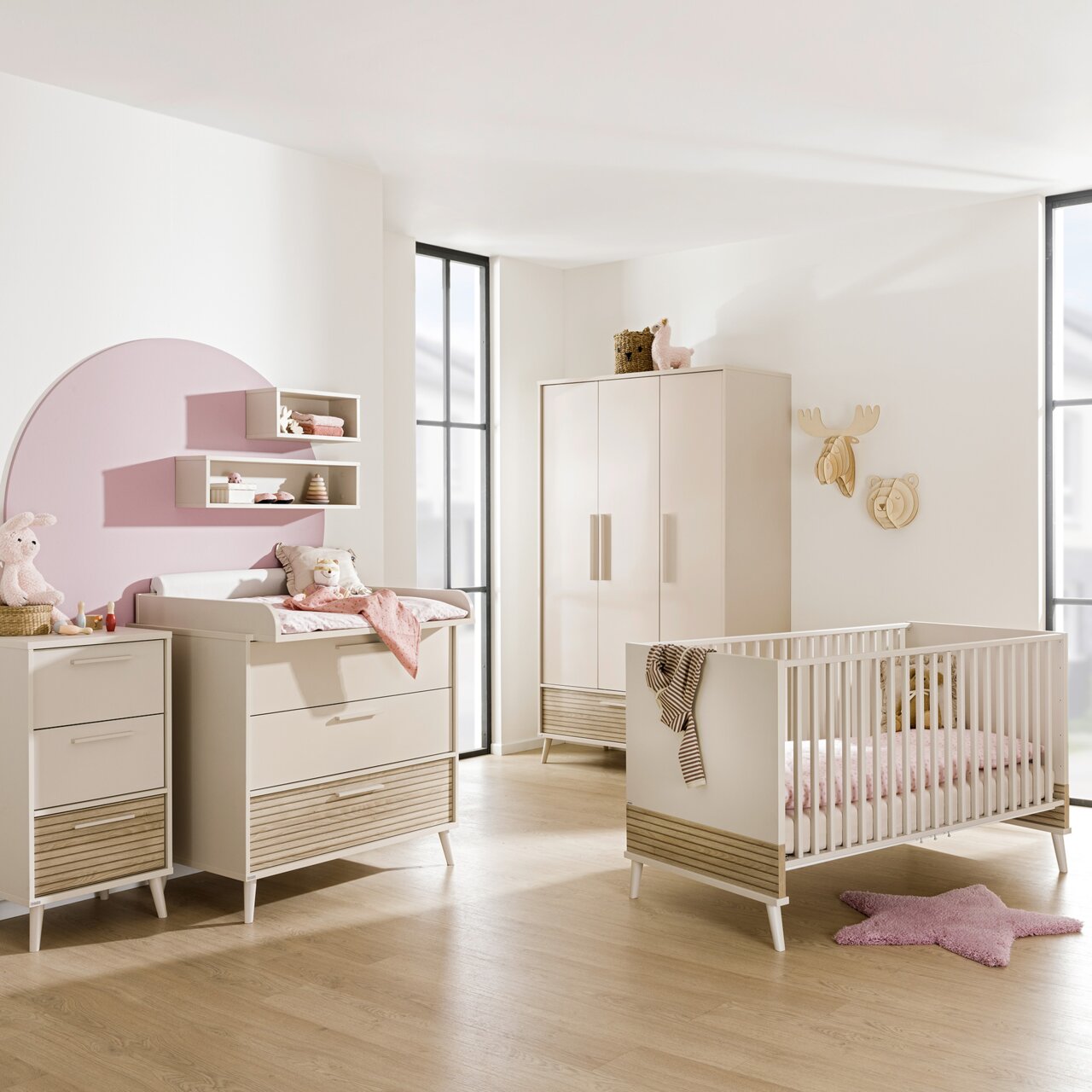 Kinderzimmer mit schmaler Kommode, Wickeltisch, Kleiderschrank und Gitterbett in hellem Holzdesign, seitliche Perspektive