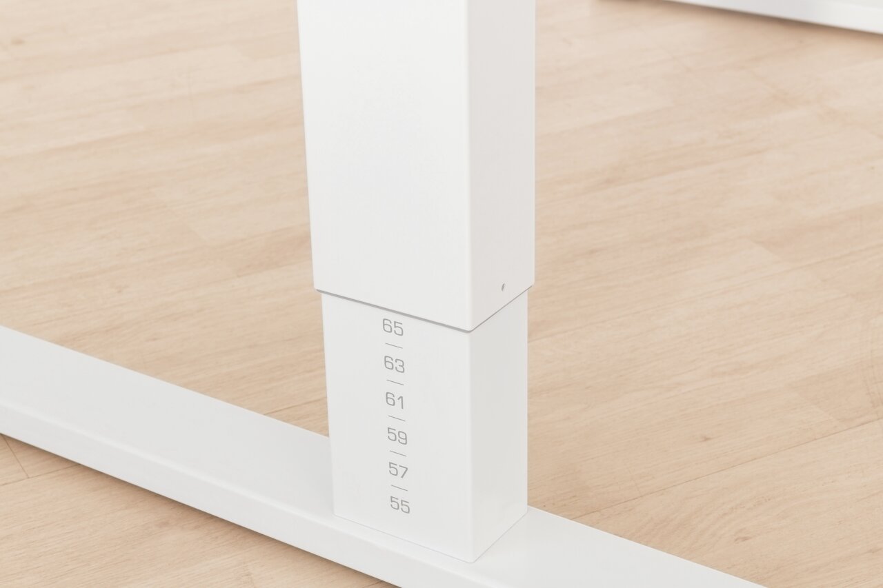Close-up van een witte, in hoogte verstelbare tafelpoot met hoogteaanduidingen op een lichte houten vloer.
