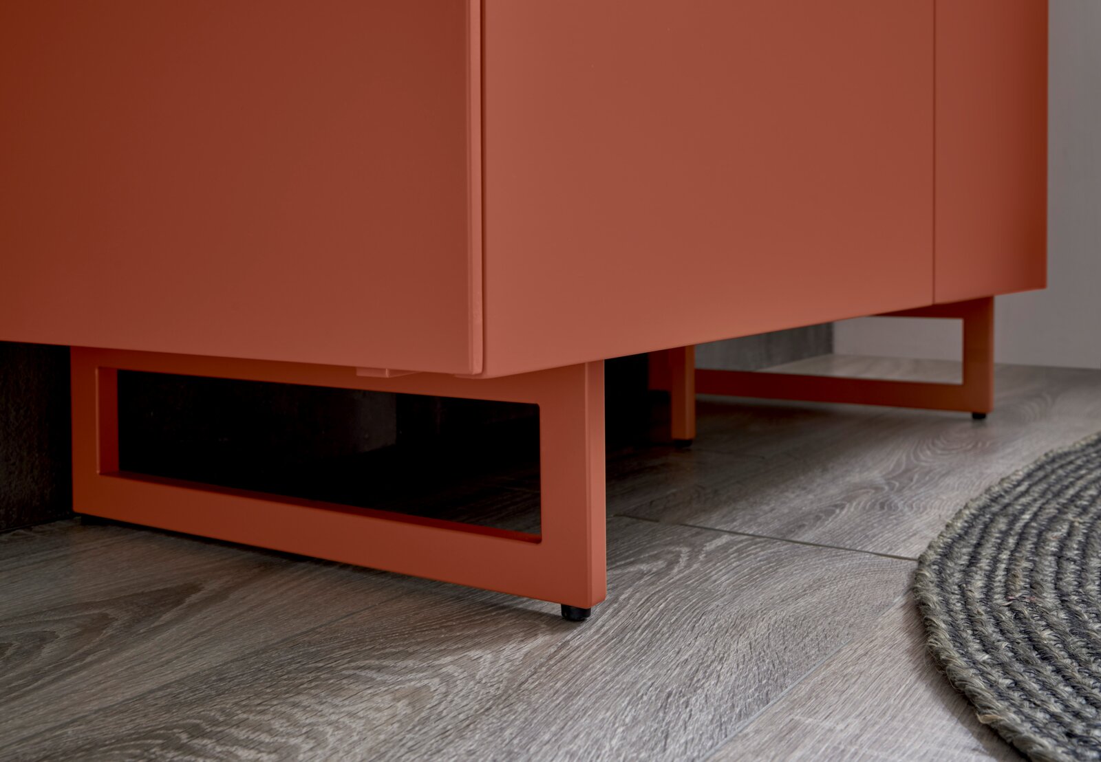 Detailaufnahme eines modernen, korallenfarbenen Sideboards/Schranks mit kastenförmigen Metallfüßen auf Holzfußboden, perspektivisch von unten schräg vorne