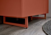 Detailaufnahme eines modernen, korallenfarbenen Sideboards/Schranks mit kastenförmigen Metallfüßen auf Holzfußboden, perspektivisch von unten schräg vorne