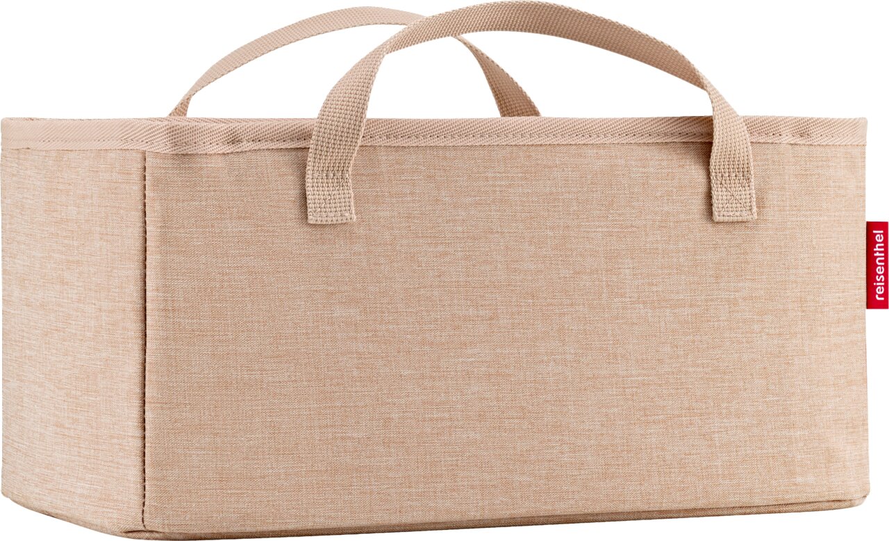Beige opbergbox van stof met twee handvatten en een rood reisenthel-label, vooraanzicht licht van bovenaf tegen een witte achtergrond.