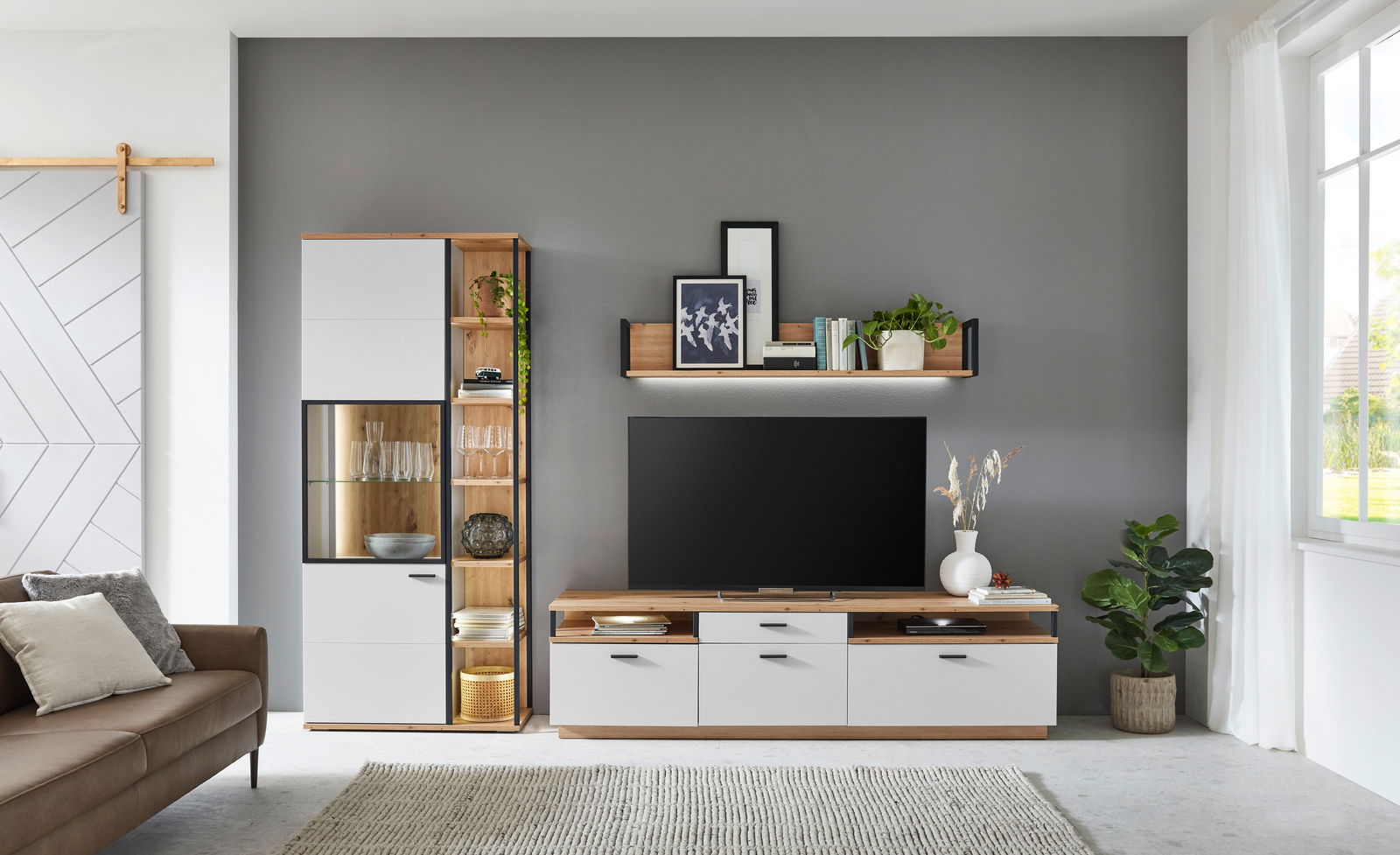 Moderne Wohnzimmer-Wandkombination in Holzoptik mit weißen Fronten, bestehend aus einem hohen Schrank, einem TV-Board und einem Wandregal, frontal fotografiert.