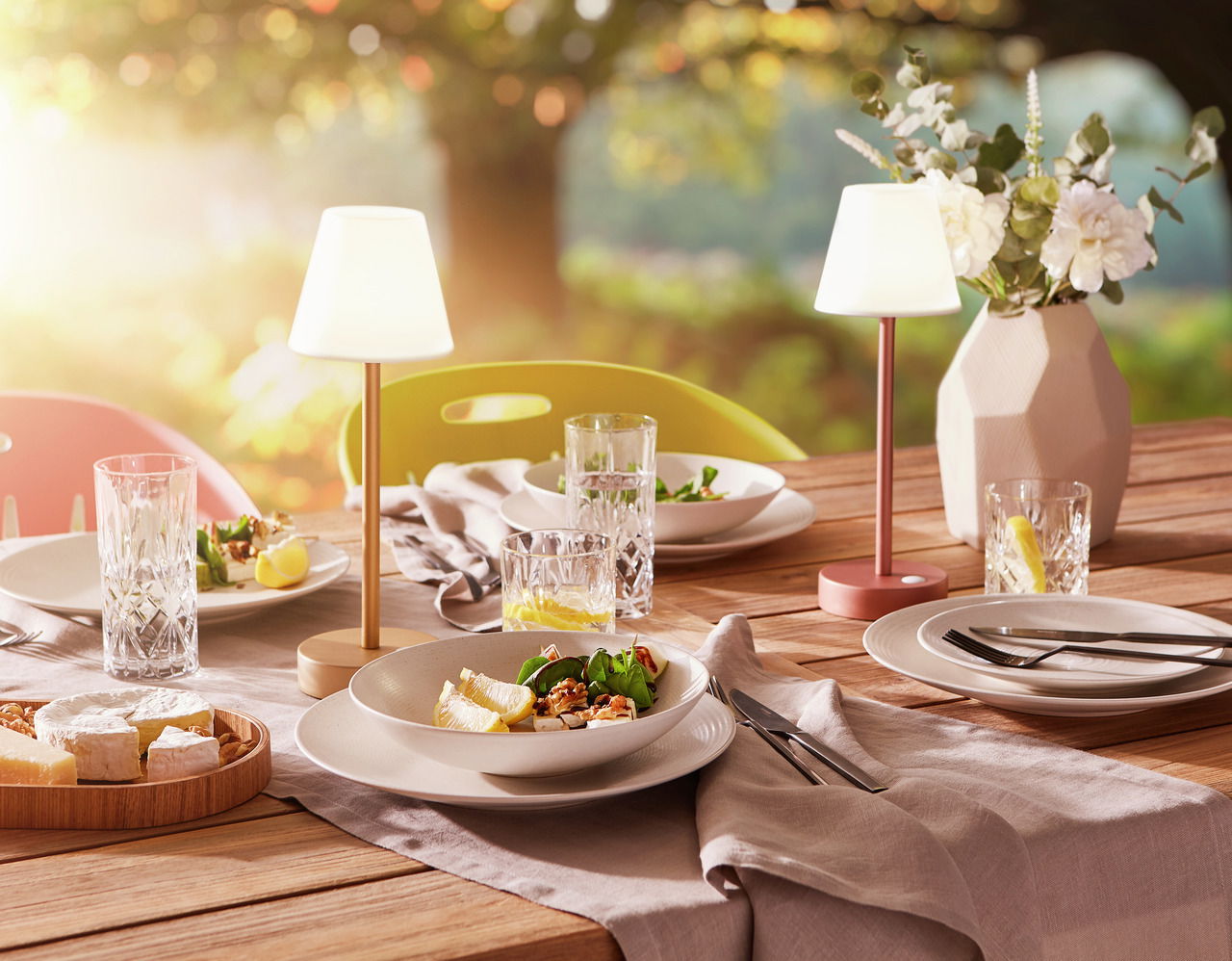 Ein stilvoll gedeckter Tisch im Freien mit dem Kombiservice Bella Vista 24-teilig, bestehend aus Tellern, Gläsern und Besteck, in einer sommerlichen Gartenszene mit warmem Sonnenlicht.