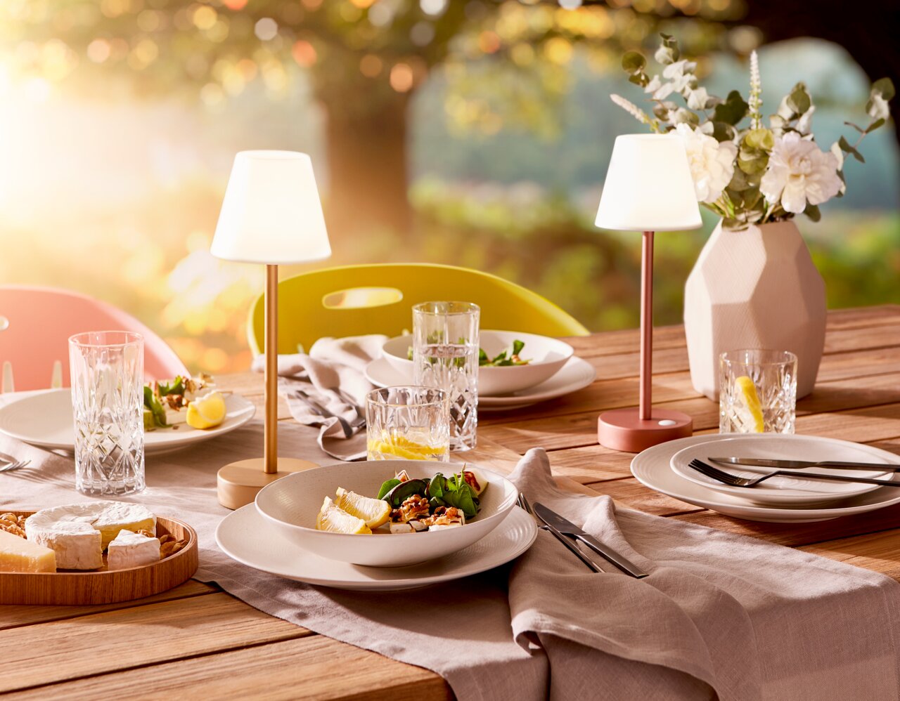 Ein stilvoll gedeckter Tisch im Freien mit dem Kombiservice Bella Vista 24-teilig, bestehend aus Tellern, Gläsern und Besteck, in einer sommerlichen Gartenszene mit warmem Sonnenlicht.