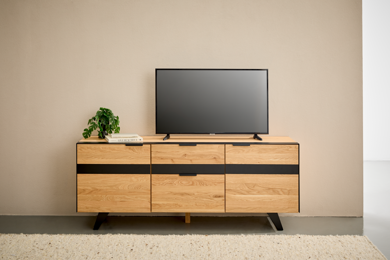 TV-Lowboard aus Holz mit schwarzem Akzent, frontal fotografiert, mit Fernseher und Pflanze dekoriert.