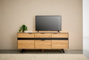 Houten tv-kast met zwarte accenten, gefotografeerd vanaf de voorkant, gedecoreerd met een tv en een plant.