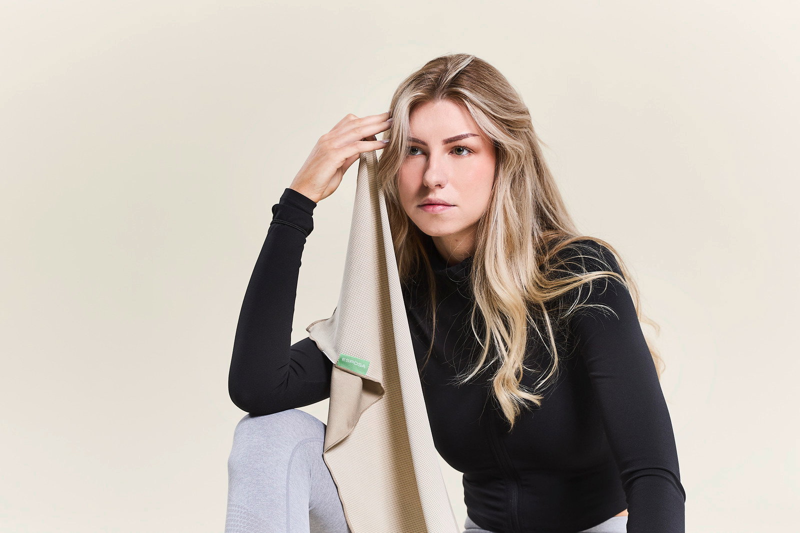 Frau in Sportkleidung hält ein beiges Sporthandtuch an ihre Stirn, seitliche Perspektive.