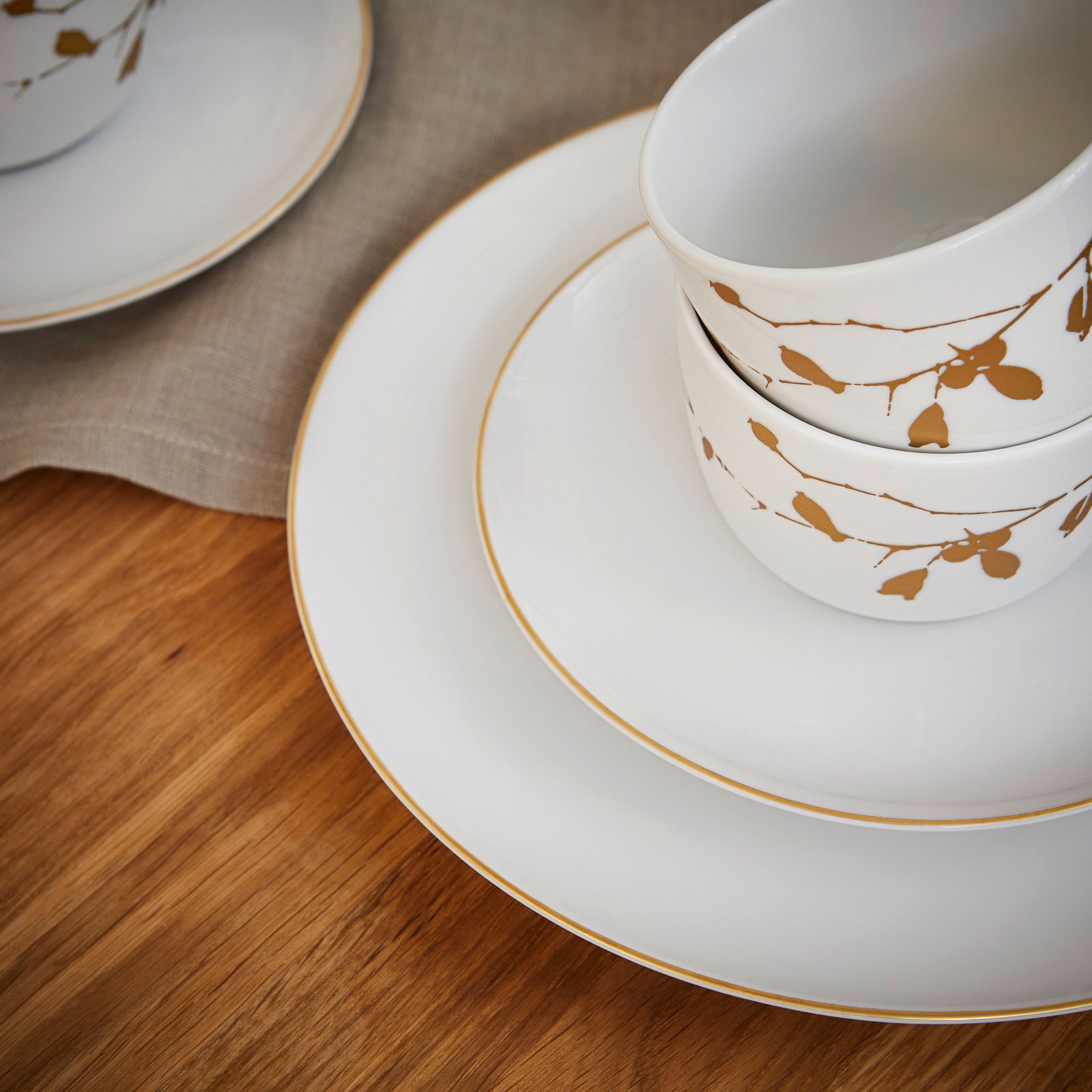 Nahaufnahme eines eleganten Kaffeeservice mit goldenen Verzierungen auf weißem Porzellan, bestehend aus Tassen und Tellern, auf einem Holztisch arrangiert.