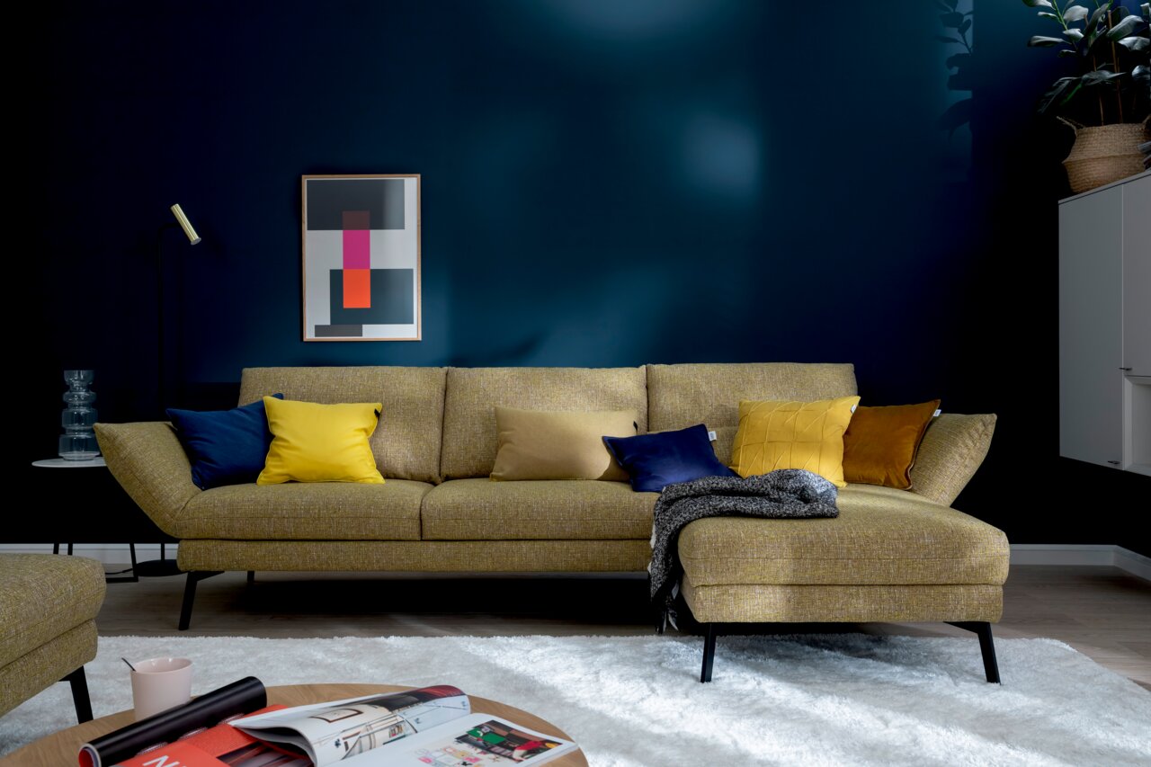 Moderne Longchairkombination in senfgelber Farbe mit bunten Kissen, frontal fotografiert in einem stilvoll eingerichteten Wohnzimmer.