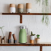 Grüne Isolierkanne 1l auf einem Regal, umgeben von Pflanzen und Keramikgefäßen, seitliche Perspektive