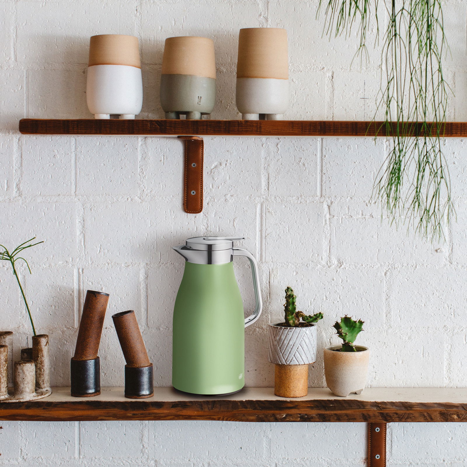 Grüne Isolierkanne 1l auf einem Regal, umgeben von Pflanzen und Keramikgefäßen, seitliche Perspektive