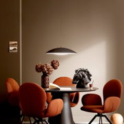 Modernes Esszimmer-Setting mit schwarzer, flacher Pendelleuchte über rundem Tisch, orangefarbenen Polsterstühlen und Deko (Vase mit Trockenblumen, Pferdekopf-Skulptur), aufgenommen in frontaler Perspektive auf Augenhöhe.