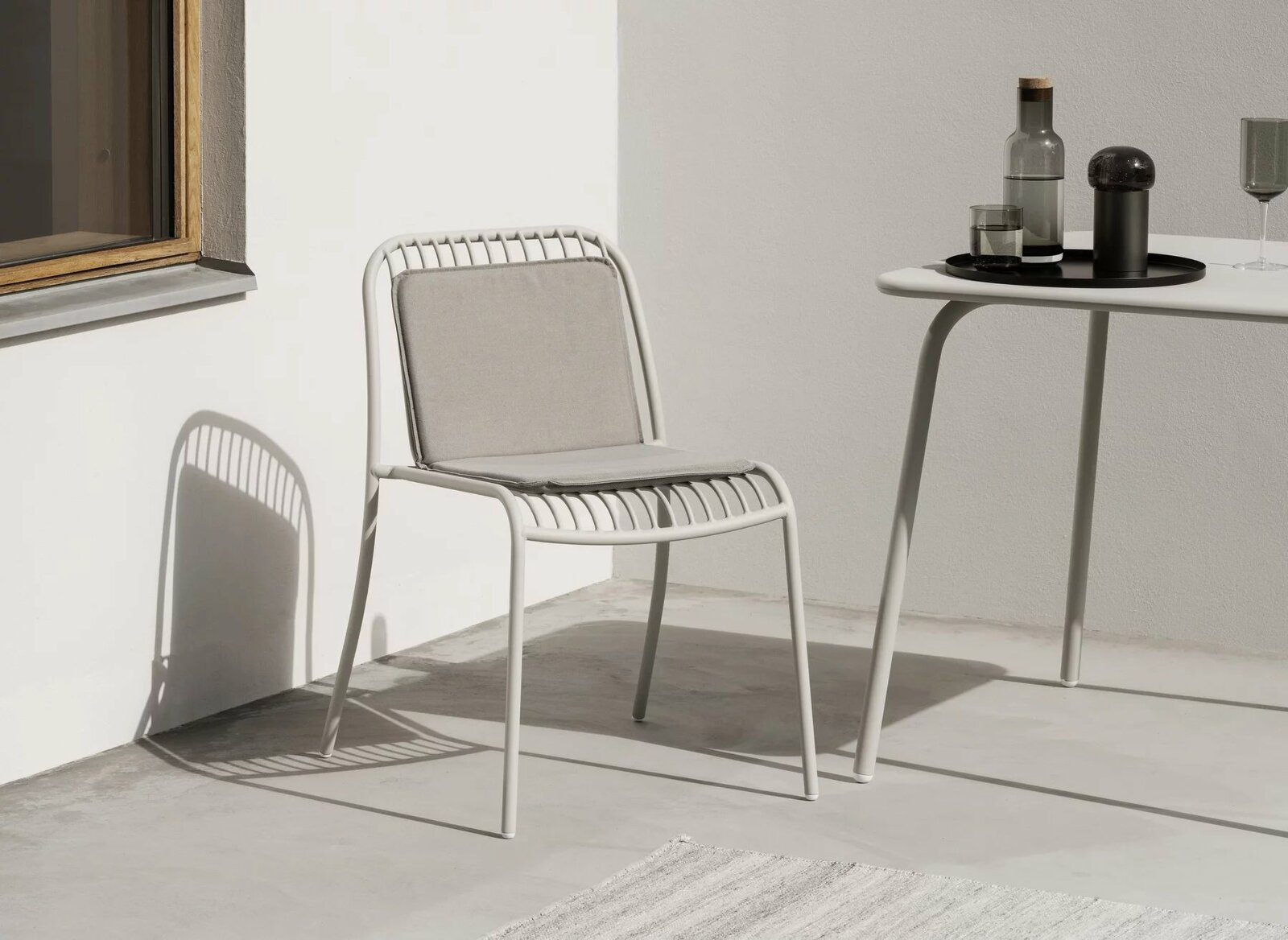 Moderner weißer Stuhl mit grauem Kissen auf einer Terrasse, seitliche Perspektive