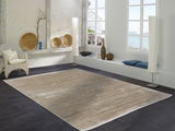 Designer Teppich in einem modernen Wohnzimmer mit Blick auf das Meer, beige und braun gestreift, auf dunklem Fliesenboden, umgeben von stilvollen Dekorationen und großen Fenstern.