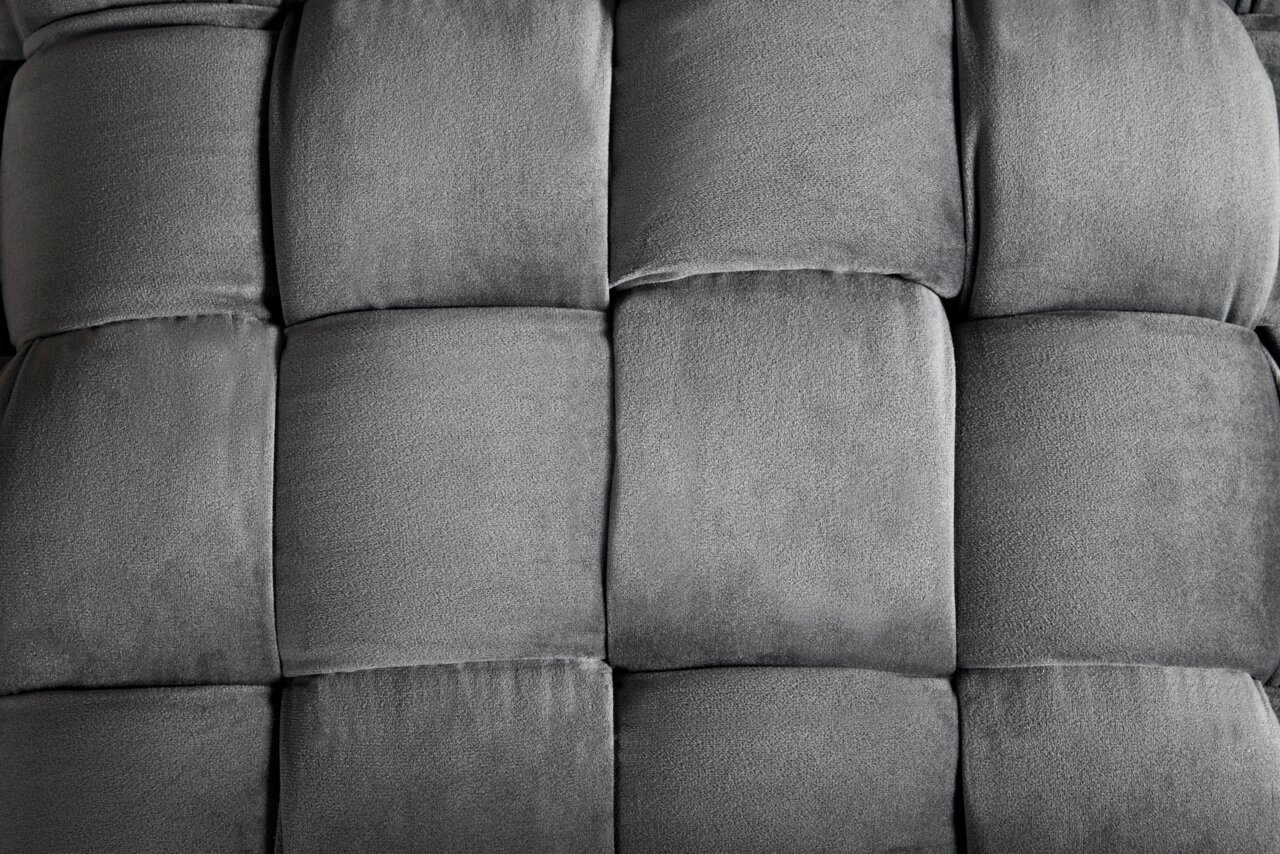 Nahaufnahme eines grauen, gepolsterten Hockers mit quadratischem Muster, von oben betrachtet.