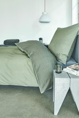 Grüne Satinbettwäsche mit Karomuster auf einem Bett, seitliche Perspektive, mit modernem Nachttisch und Dekoration.