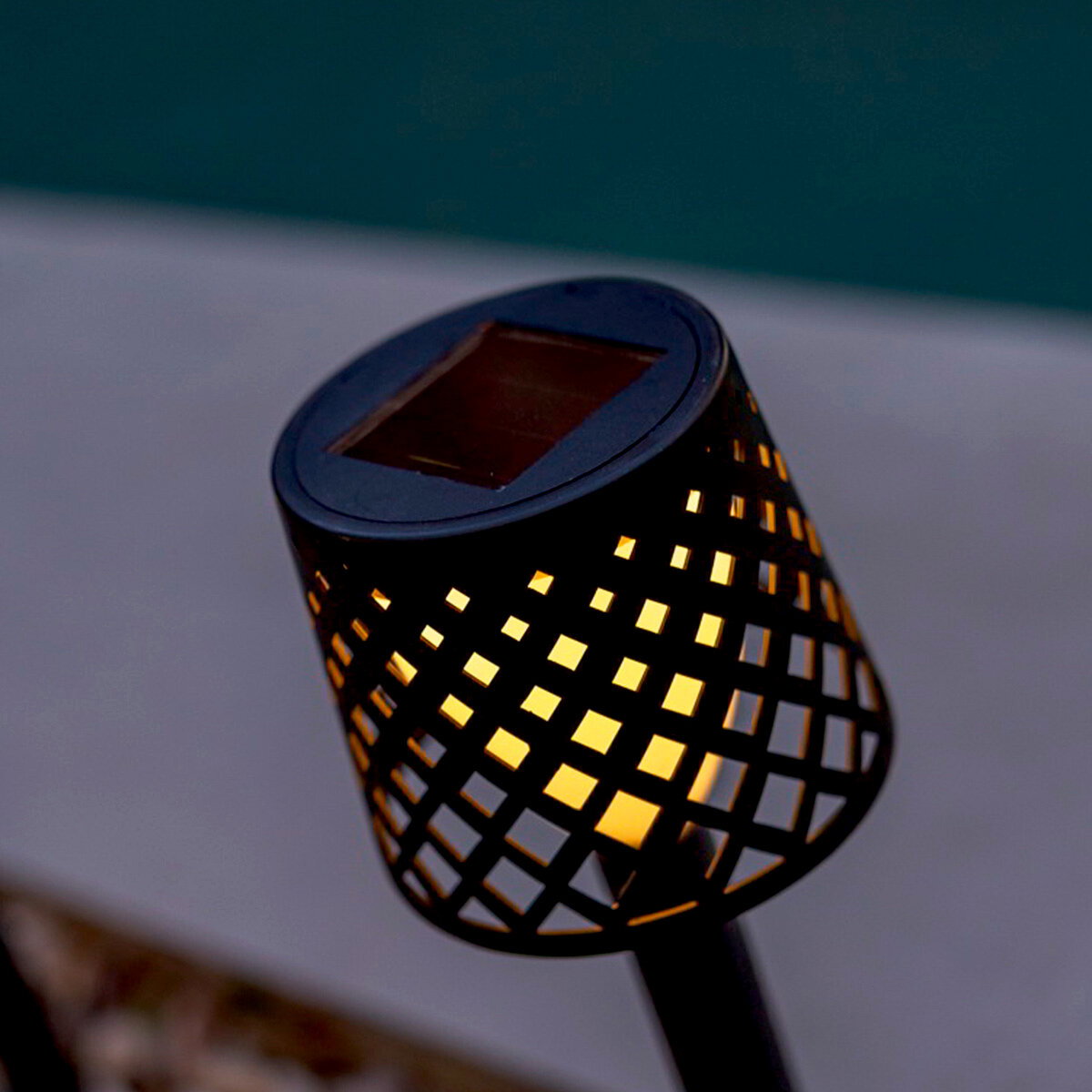 Schwarze Solar-Gartenleuchte mit warmem Licht und perforiertem Gittermuster, schräg von oben in Nahaufnahme fotografiert