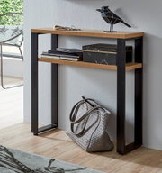 Schmaler Konsolentisch im Industrial-Design mit Holzoptik-Ablageflächen und schwarzem Metallgestell an einer grauen Wand, mit Deko und Tasche darunter, fotografiert in frontaler leicht seitlicher Perspektive.