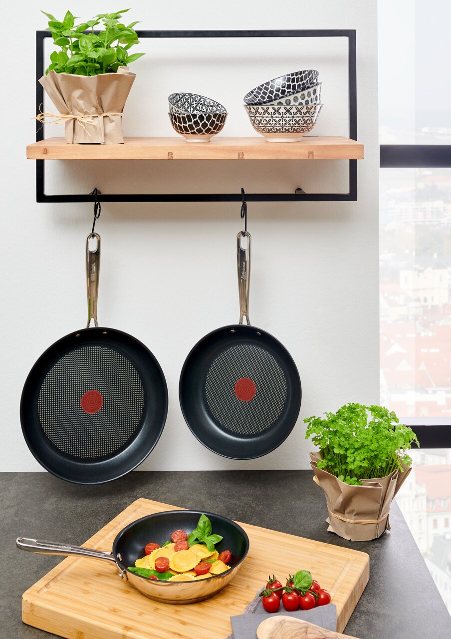 Drie Jamie Oliver Smart-koekenpannen, twee hangend en één op een snijplank met ravioli en tomaten, gezien van voren.