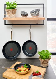 Drie Jamie Oliver Smart-koekenpannen, twee hangend en één op een snijplank met ravioli en tomaten, gezien van voren.