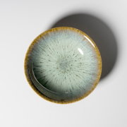 Runde Keramikschale mit hellblauer reaktiver Glasur und braunem Rand auf weißem Hintergrund, Draufsicht von oben
