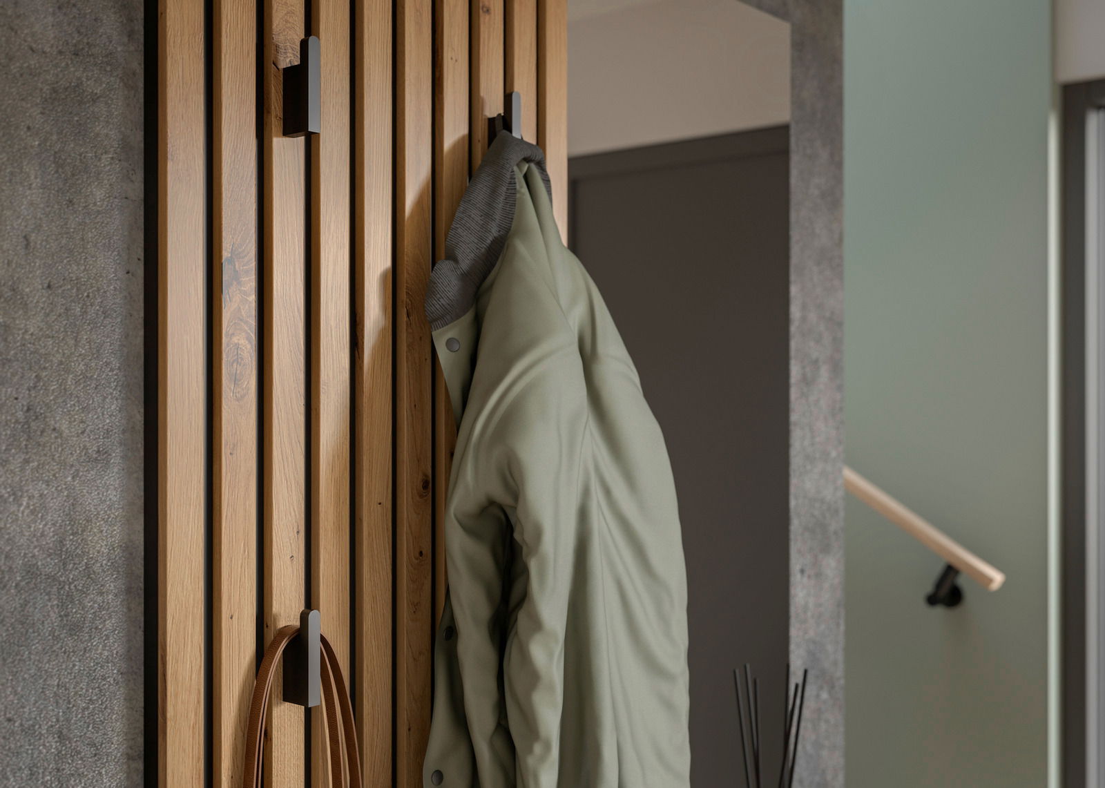 Nahaufnahme einer Kompaktgarderobe aus Holz mit mehreren Haken, an denen eine grüne Jacke hängt. Perspektive von der Seite.
