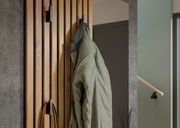 Nahaufnahme einer Kompaktgarderobe aus Holz mit mehreren Haken, an denen eine grüne Jacke hängt. Perspektive von der Seite.