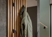 Nahaufnahme einer Kompaktgarderobe aus Holz mit mehreren Haken, an denen eine grüne Jacke hängt. Perspektive von der Seite.