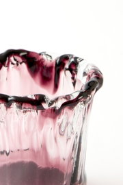 Close-up vanuit een licht verhoogd zijaanzicht van een mondgeblazen roze glazen vaas met organisch golvende rand en donkerpaarse accenten.