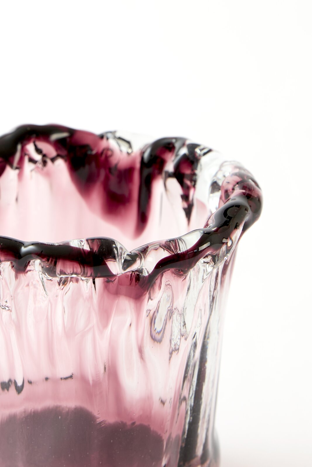 Close-up vanuit een licht verhoogd zijaanzicht van een mondgeblazen roze glazen vaas met organisch golvende rand en donkerpaarse accenten.
