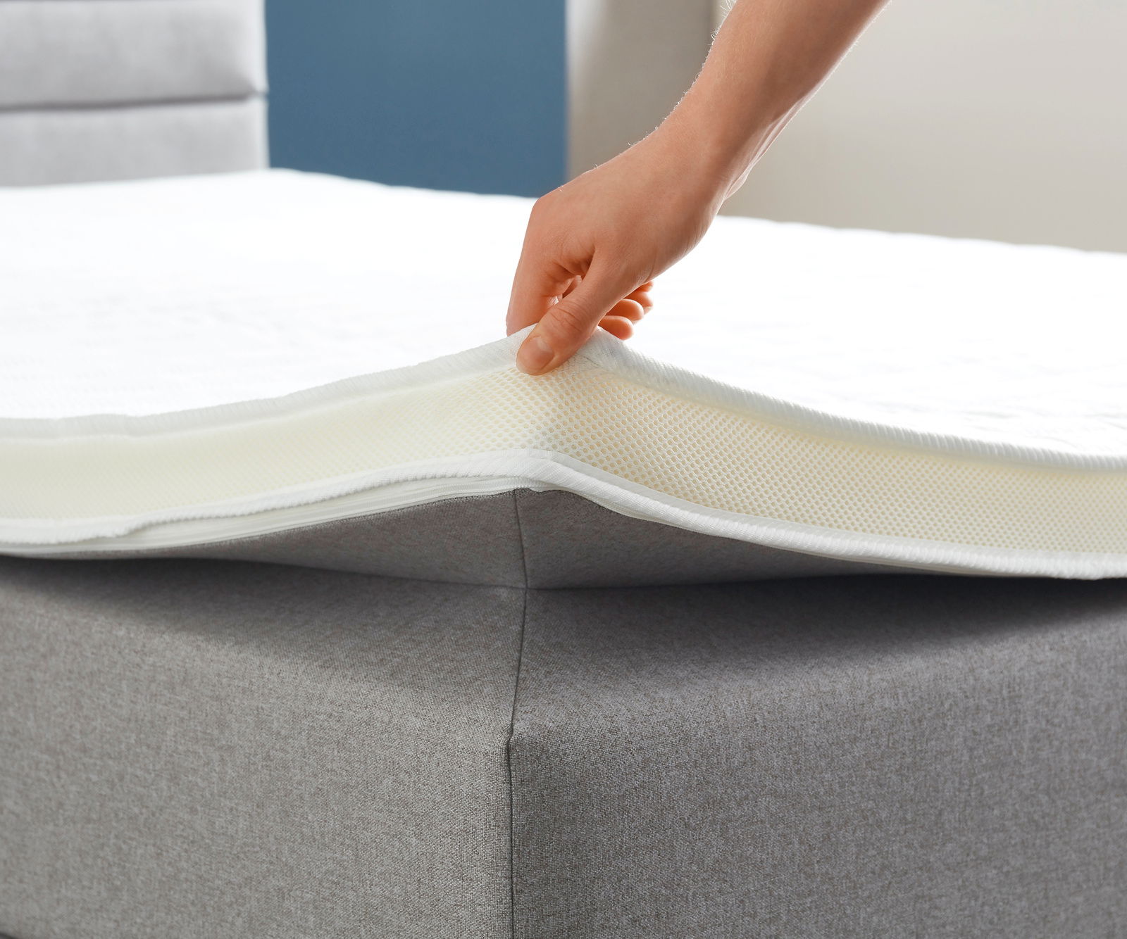 Nahaufnahme eines Boxspringbetts mit einer Hand, die die Matratze anhebt, um die Schichten zu zeigen.