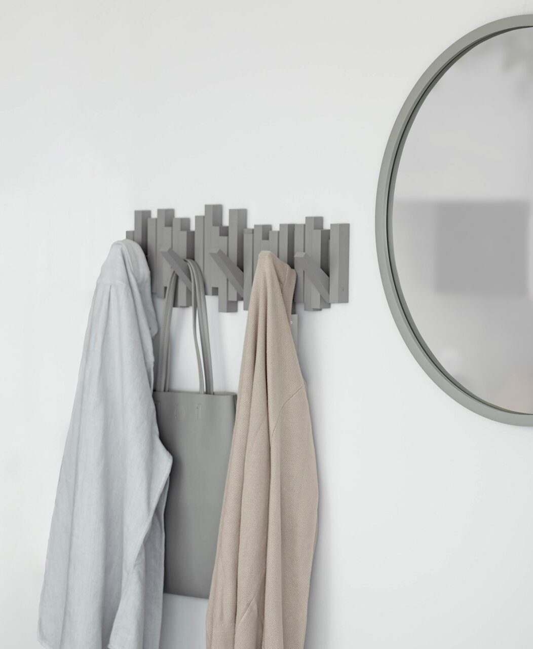 Moderne Wandgarderobe mit mehreren Haken, an der Kleidung und eine Tasche hängen. Perspektive von vorne.