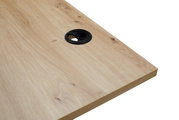 Nahaufnahme einer Schreibtischplatte aus hellem Holz mit Kabeldurchlass, perspektivisch von oben rechts fotografiert.