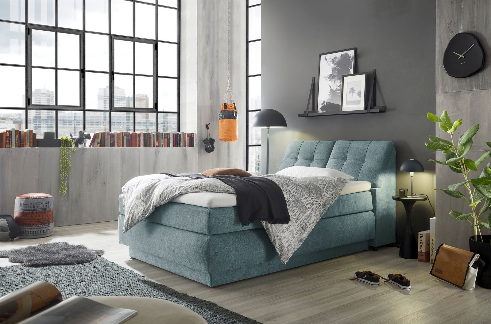 Boxspringbett in modernem Schlafzimmer mit großen Fenstern, grauer Wand und stilvoller Dekoration, seitliche Perspektive