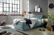 Boxspringbett in modernem Schlafzimmer mit großen Fenstern, grauer Wand und stilvoller Dekoration, seitliche Perspektive