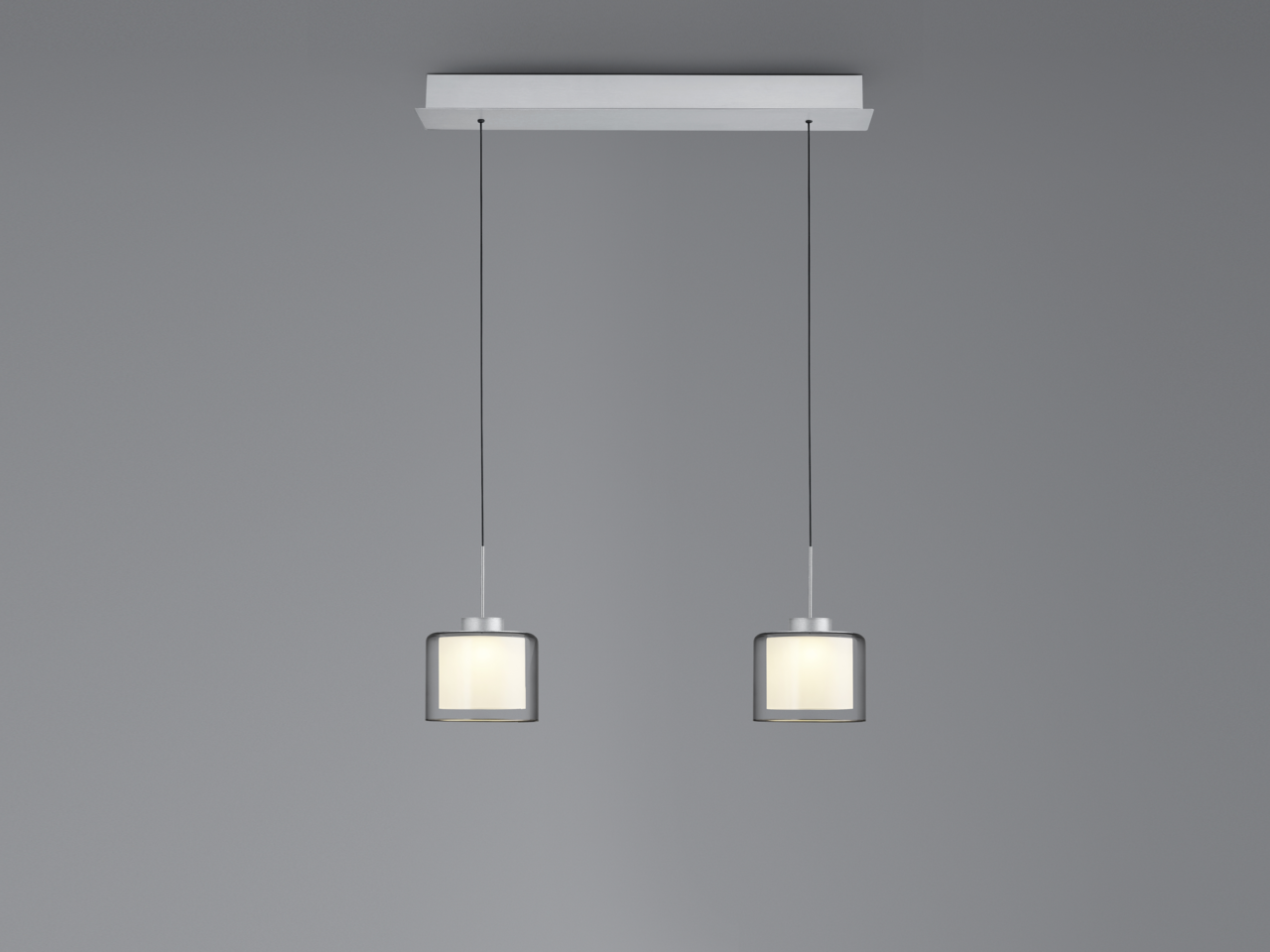 Moderne LED-Pendelleuchte mit zwei zylindrischen Lampenschirmen, hängend an dünnen Kabeln von einer rechteckigen Deckenhalterung, seitliche Perspektive.