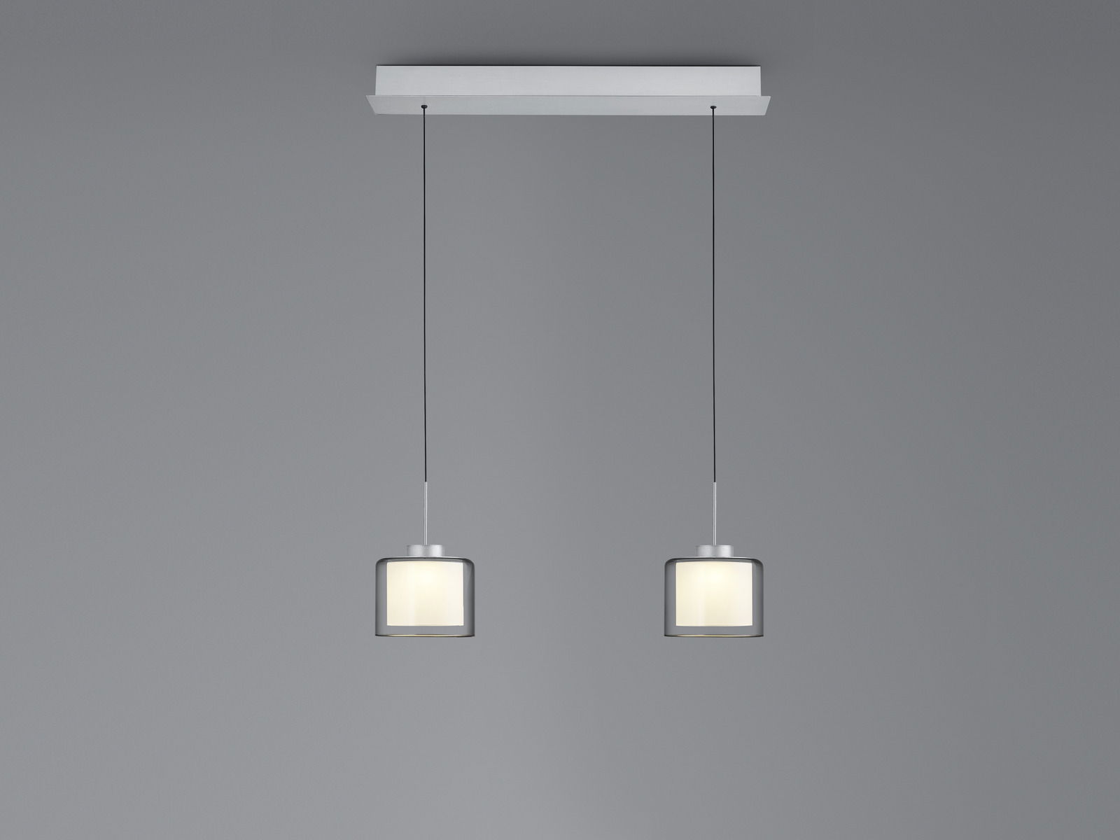 Moderne LED-Pendelleuchte mit zwei zylindrischen Lampenschirmen, hängend an dünnen Kabeln von einer rechteckigen Deckenhalterung, seitliche Perspektive.