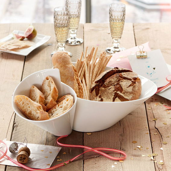 Villeroy & Boch Eye-Catcher BOL 49x27cm NEW WAVE Doppelschale aus weißem Porzellan, gefüllt mit verschiedenen Brotsorten, auf einem rustikalen Holztisch. Perspektive von oben.