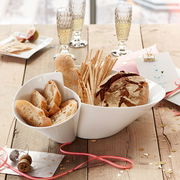 Doppelschale aus weißem Porzellan, gefüllt mit verschiedenen Brotsorten, auf einem rustikalen Holztisch. Perspektive von oben.