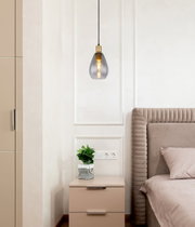 Moderne Hängeleuchte mit rauchgrauem Glasschirm und goldener Fassung, von der Seite betrachtet, über einem Nachttisch in einem stilvollen Schlafzimmer.
