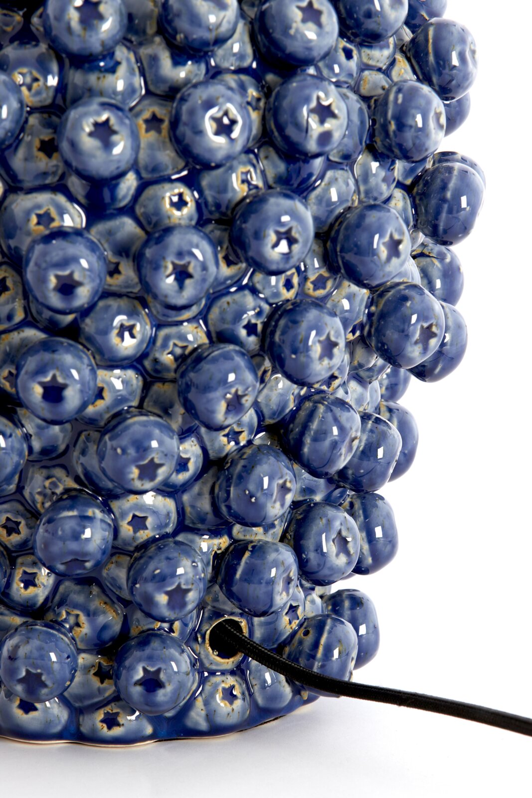 Nahaufnahme eines blauen, strukturierten Lampenfußes mit runden, glänzenden Erhebungen und einem Kabel, das aus der Seite herausragt.