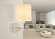 Moderne Wandleuchte mit zylindrischem Stoffschirm, seitliche Perspektive, montiert in einem stilvollen Wohnzimmer.