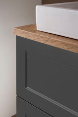 Nahaufnahme eines Waschtisch-Sets mit weißem Waschbecken und dunklem Unterschrank mit Holzoberfläche, seitliche Perspektive.