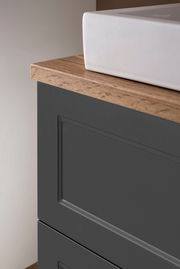 Nahaufnahme eines Waschtisch-Sets mit weißem Waschbecken und dunklem Unterschrank mit Holzoberfläche, seitliche Perspektive.