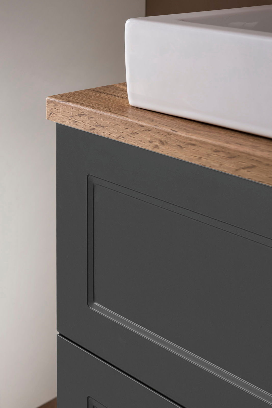 Nahaufnahme eines Waschtisch-Sets mit weißem Waschbecken und dunklem Unterschrank mit Holzoberfläche, seitliche Perspektive.