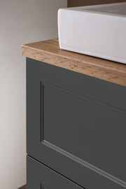 Nahaufnahme eines Waschtisch-Sets mit weißem Waschbecken und dunklem Unterschrank mit Holzoberfläche, seitliche Perspektive.