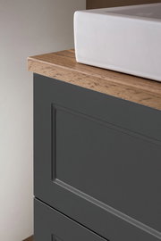 Nahaufnahme eines Waschtisch-Sets mit weißem Waschbecken und dunklem Unterschrank mit Holzoberfläche, seitliche Perspektive.