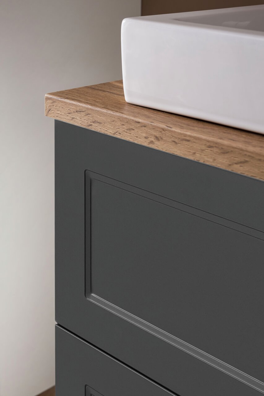 Nahaufnahme eines Waschtisch-Sets mit weißem Waschbecken und dunklem Unterschrank mit Holzoberfläche, seitliche Perspektive.
